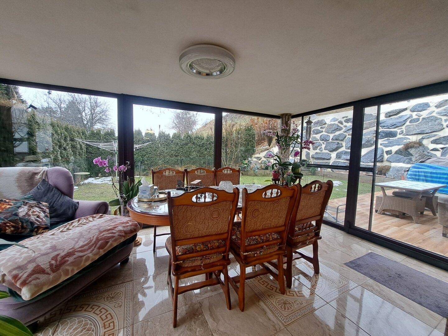 Heller Wintergarten mit Esstisch, großen Glasflächen und direktem Blick in den Gartenbereich.