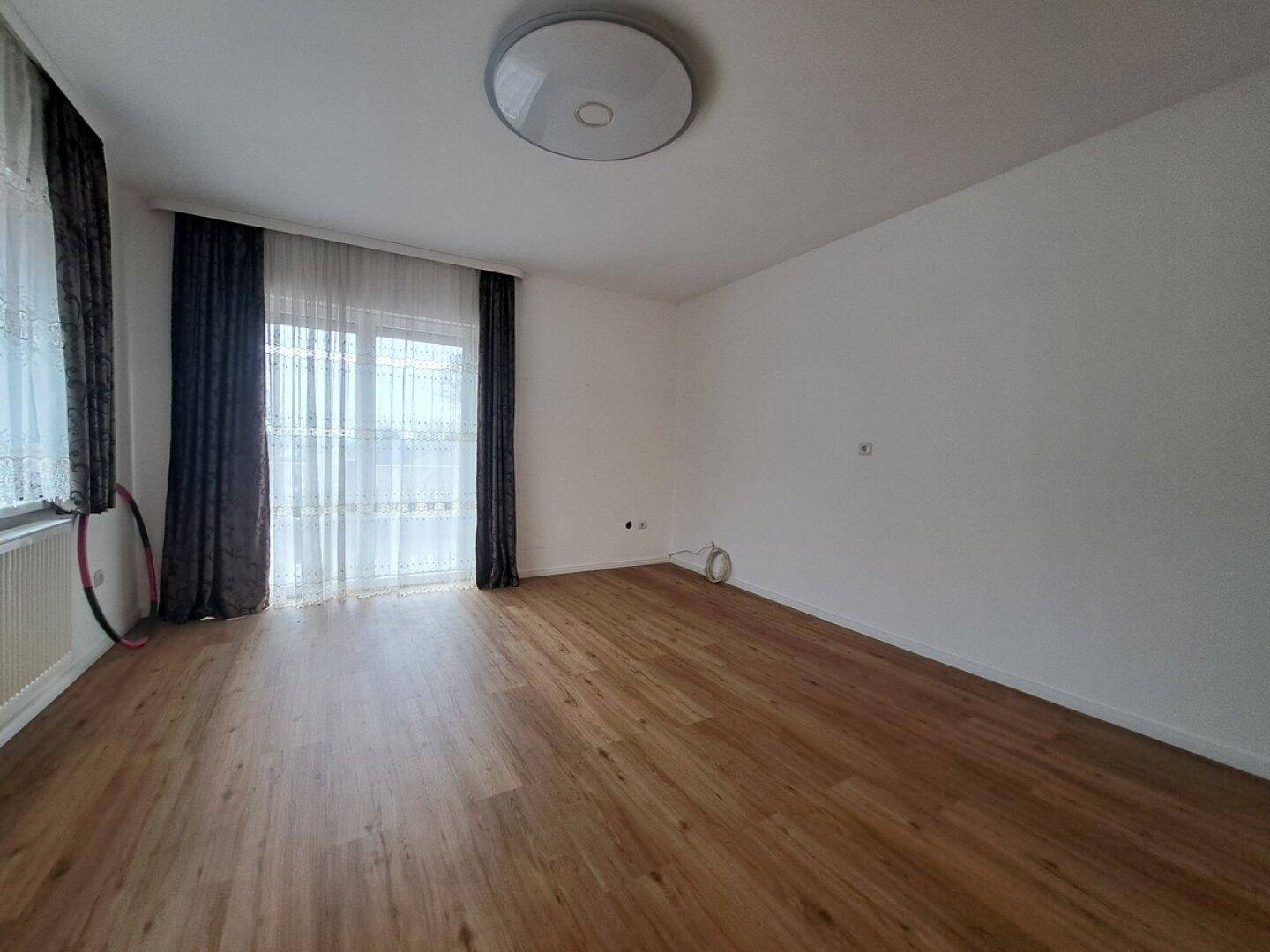 Helles Zimmer mit Laminatboden und Zugang zu einem Balkon oder einer Terrasse durch eine große Tür.