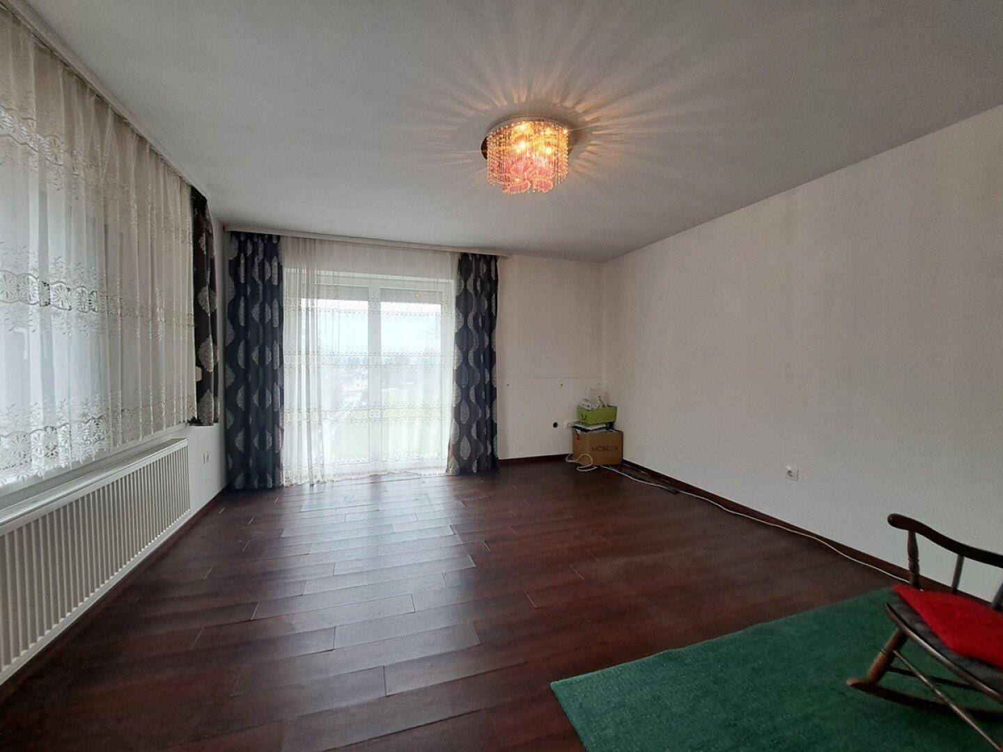 Helles Zimmer mit dunklem Laminatboden und großem Fenster mit Vorhängen, ideal für Tageslicht.