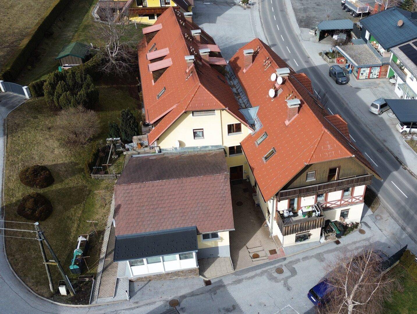 Luftaufnahme eines Wohnkomplexes mit mehreren Gebäudeteilen, roten Dächern und angrenzender Straße.