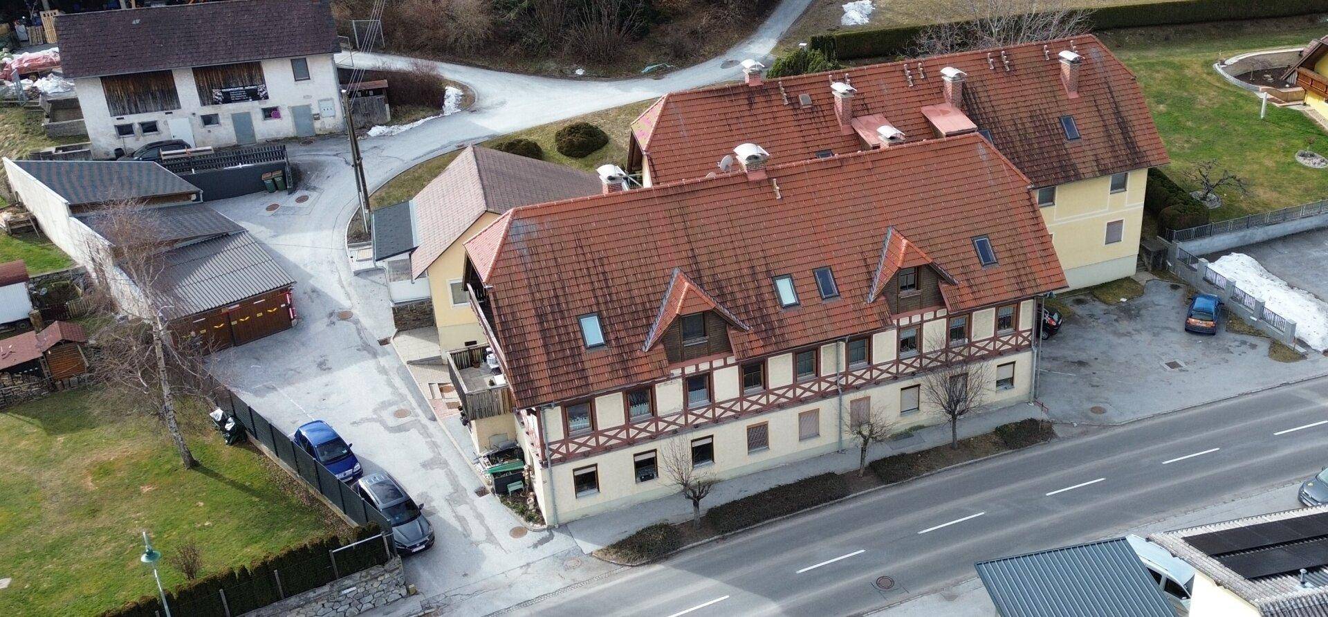 Weitläufige Luftansicht eines traditionellen Wohnhauses mit rotem Ziegeldach und angrenzender Straße.