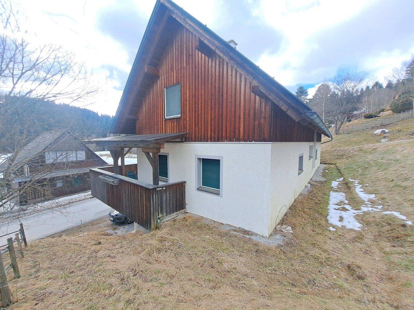 Ansicht des Hauses mit Holzbalkon und weißer Fassade in ländlicher Umgebung.