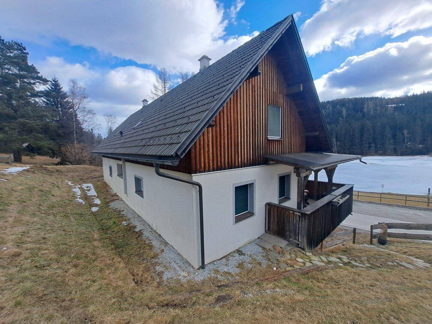 Seitenansicht des Hauses mit weißer Fassade und Holzelementen nahe einem See.