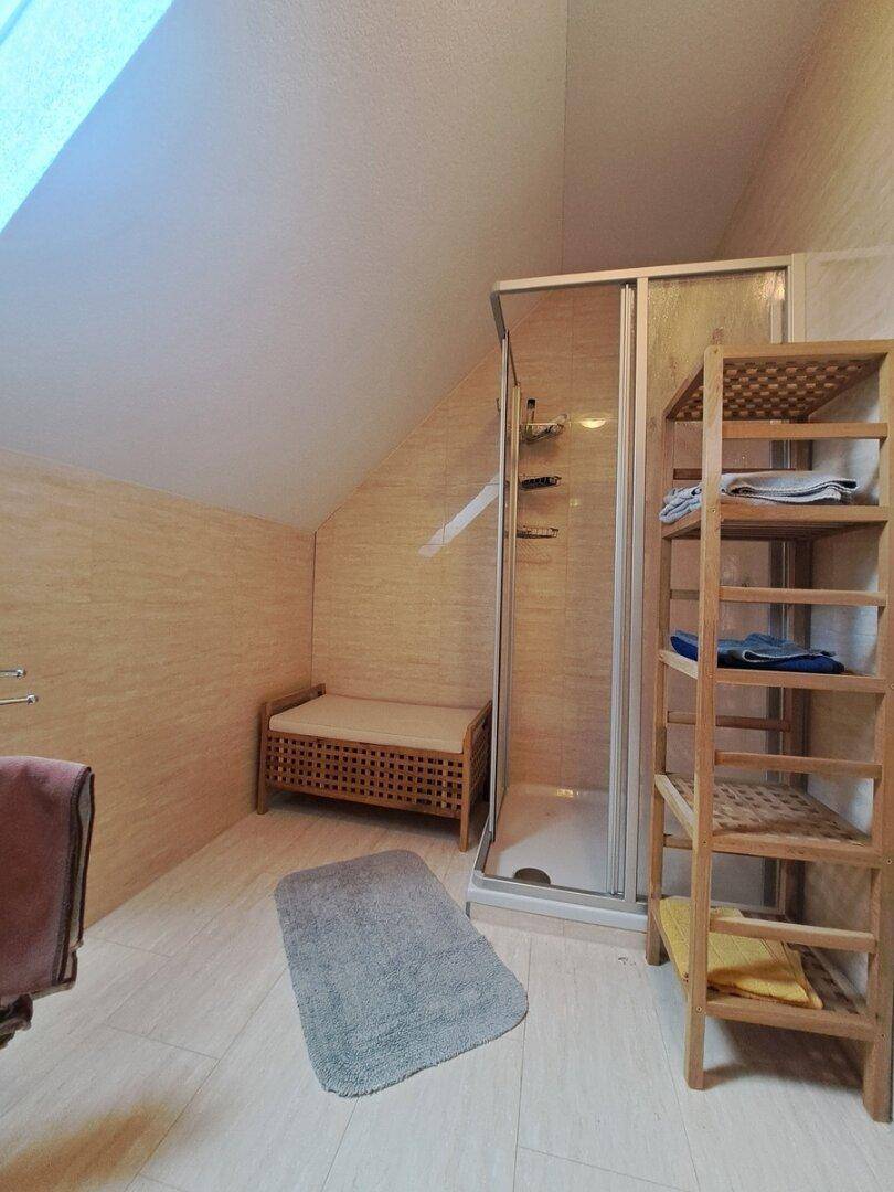 Badezimmer im Dachgeschoss mit Dusche, Holzregal und schrägen Wänden.