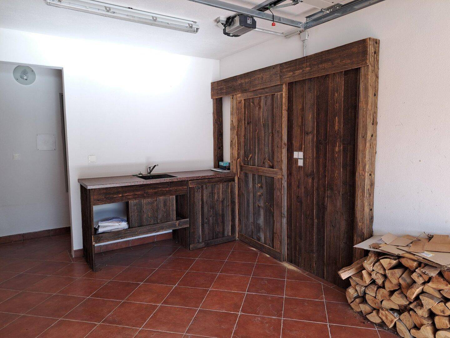 Geräumige Garage mit Werkbank, Spülbecken und Holzstapel.