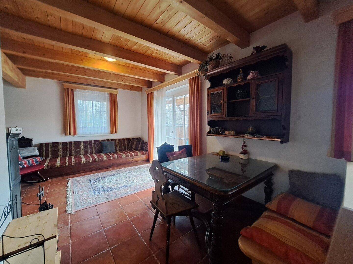 Rustikaler Wohnbereich mit Holzbalkendecke, Esstisch und traditionellem Sofa.