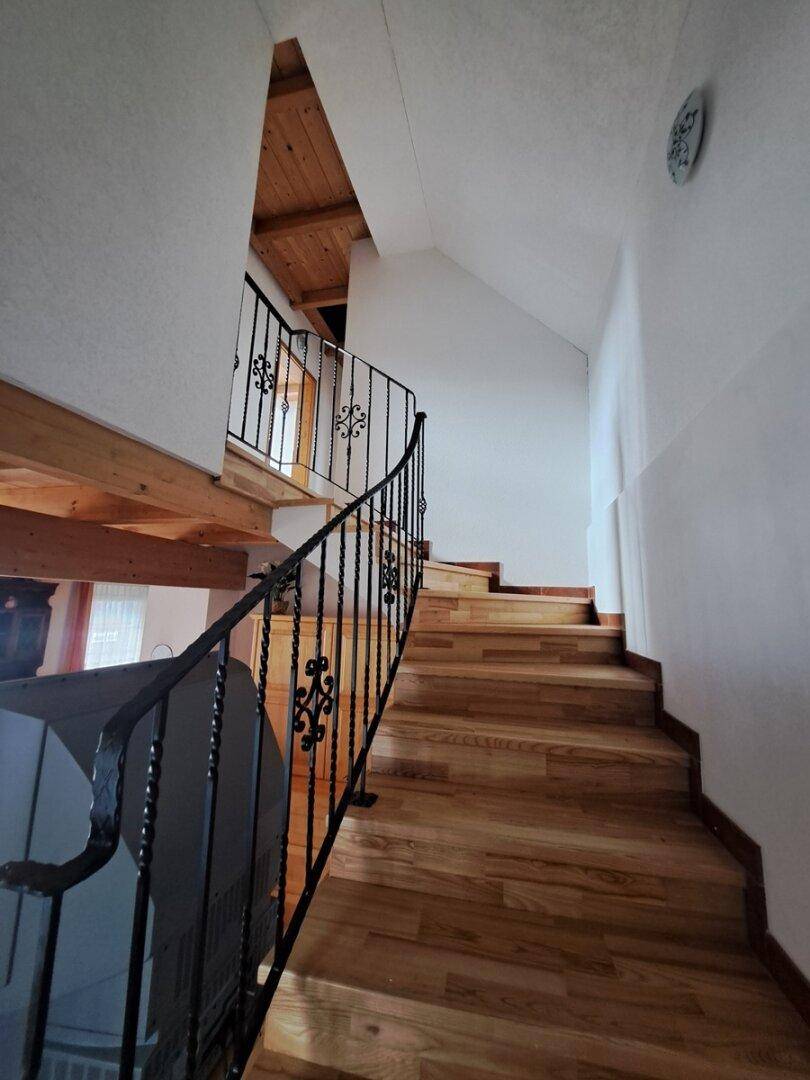 Holztreppe mit schmiedeeisernem Geländer führt in das obere Stockwerk.