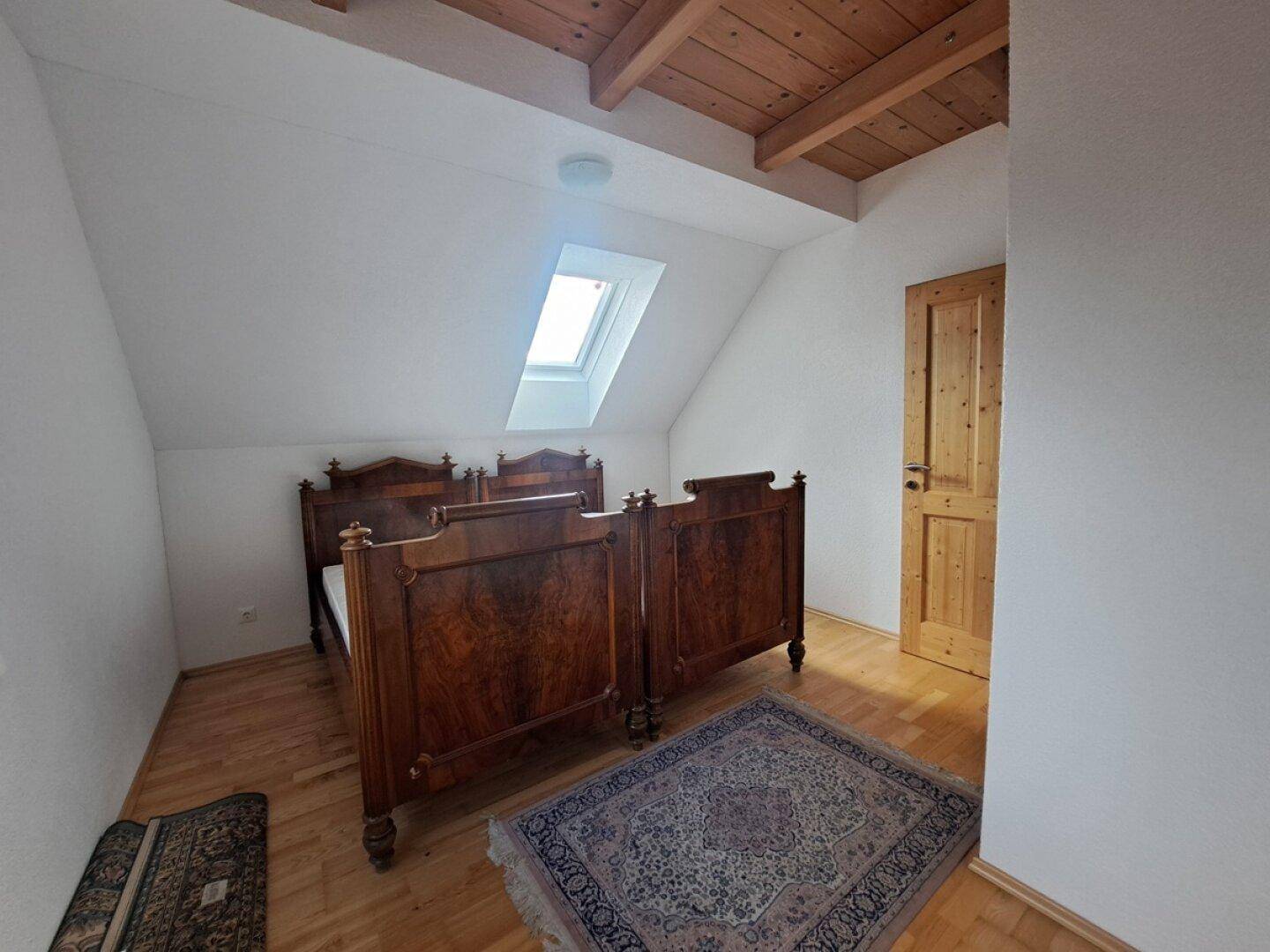 Schlafzimmer im Dachgeschoss mit zwei Betten, Holzboden und Dachfenster.