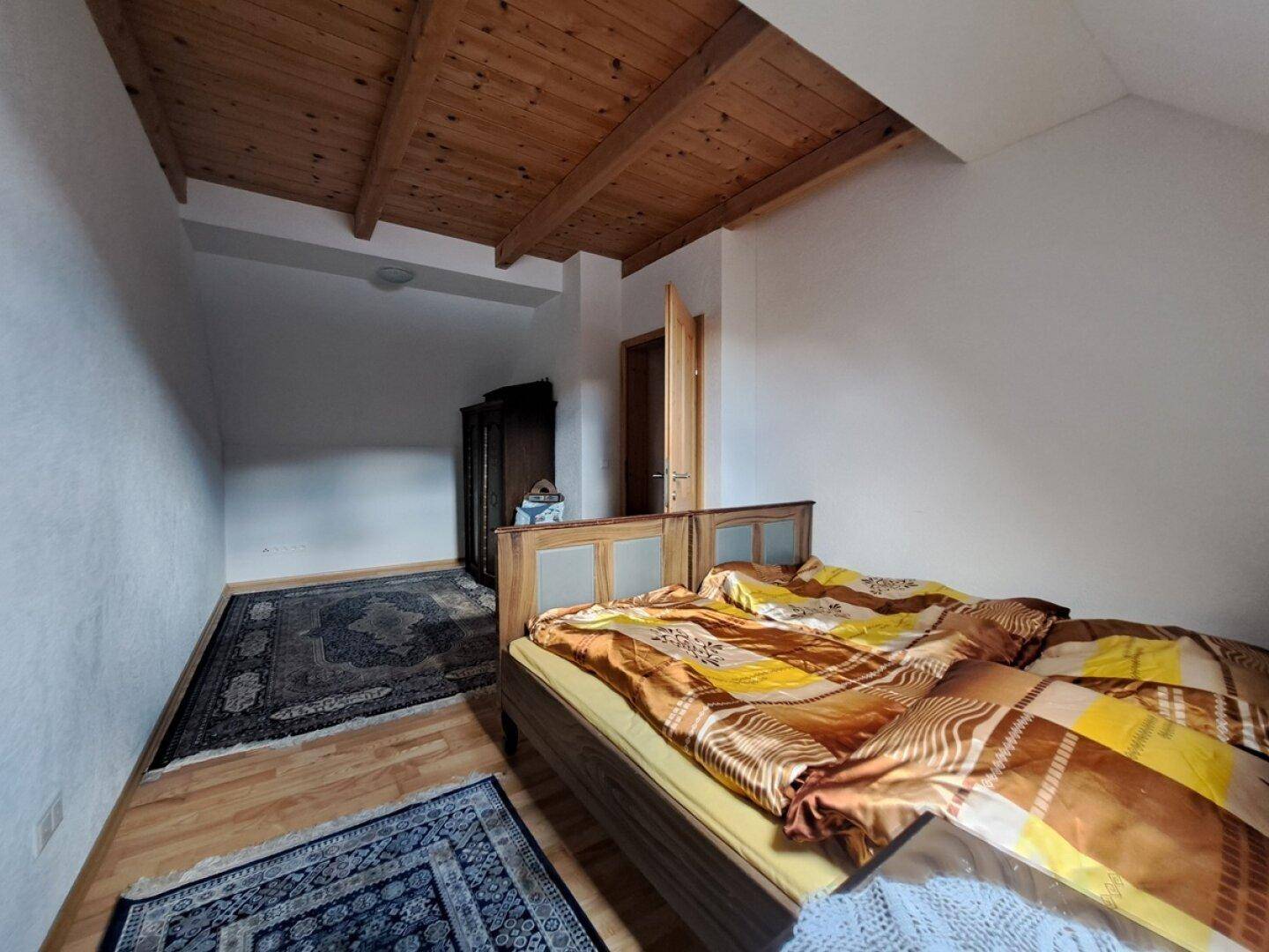 Schlafzimmer mit Holzbalkendecke, Doppelbett und Teppichen auf dem Holzboden.