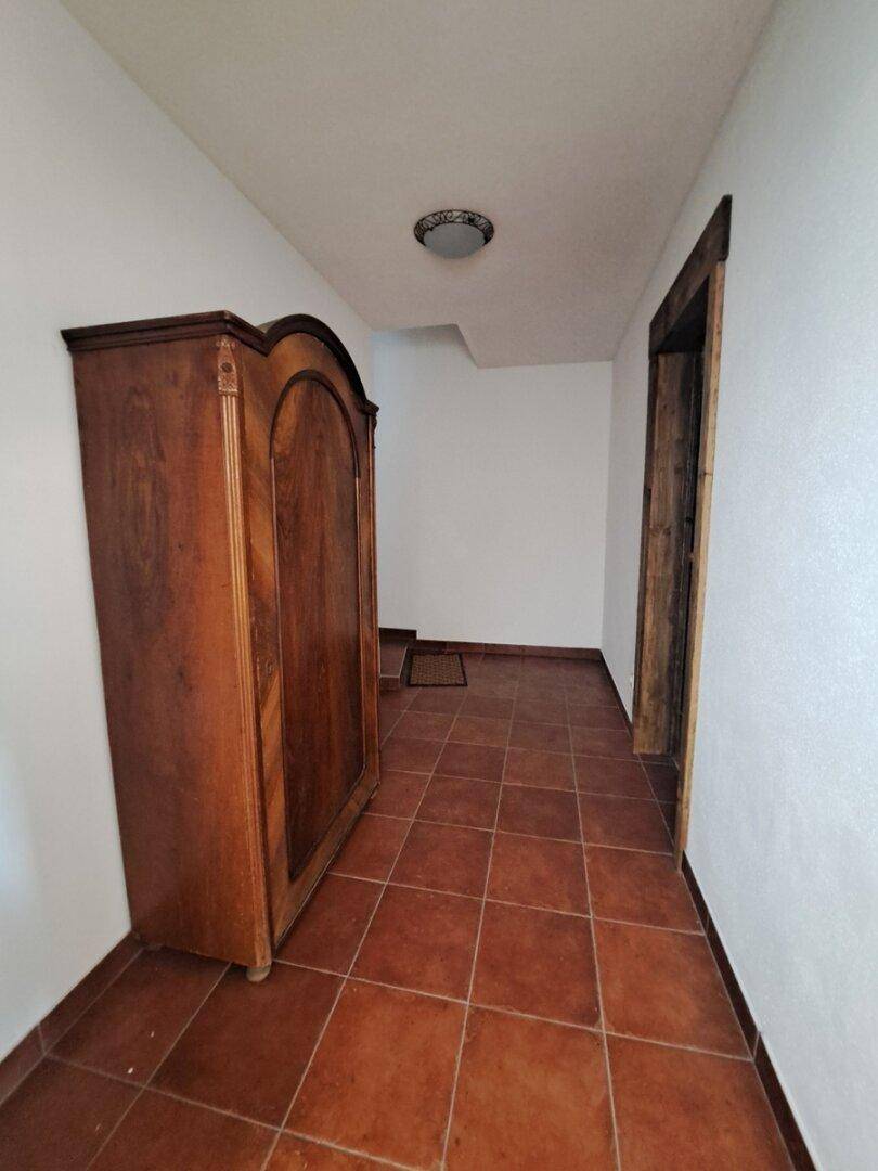 Flur mit Terrakottafliesen und einem antiken Holzschrank.