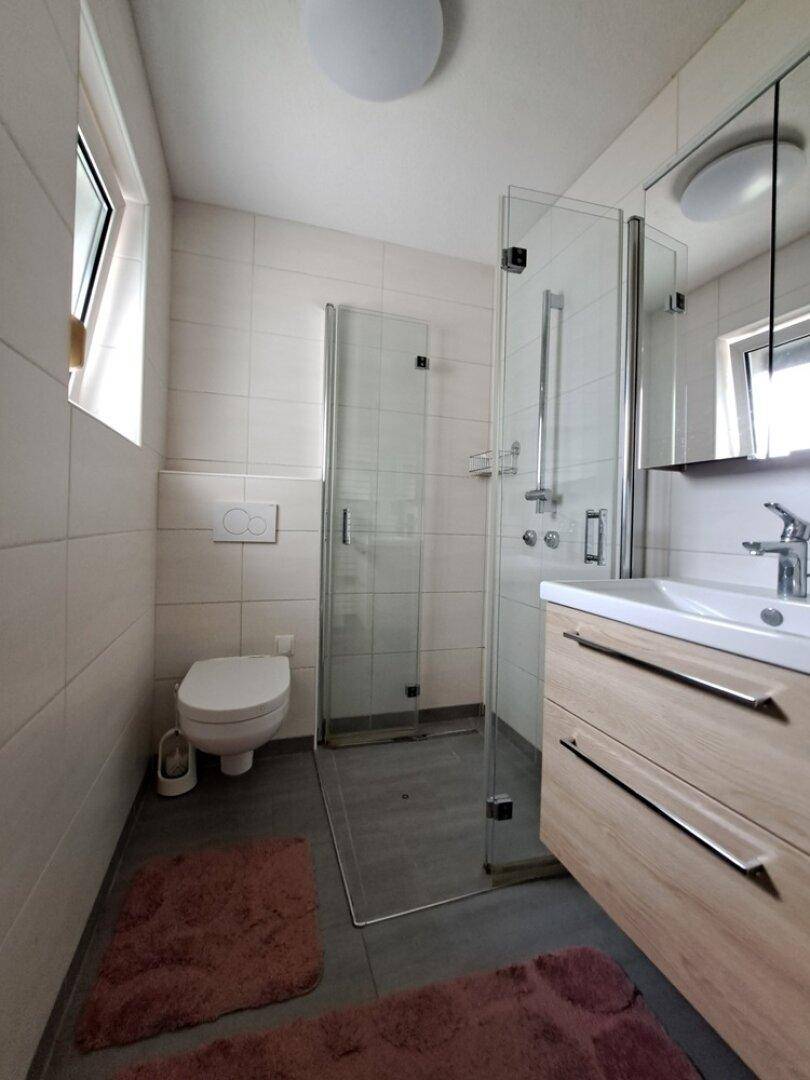 Modernes Badezimmer mit Duschkabine, wandhängendem WC, Waschtischunterschrank und Fenster.