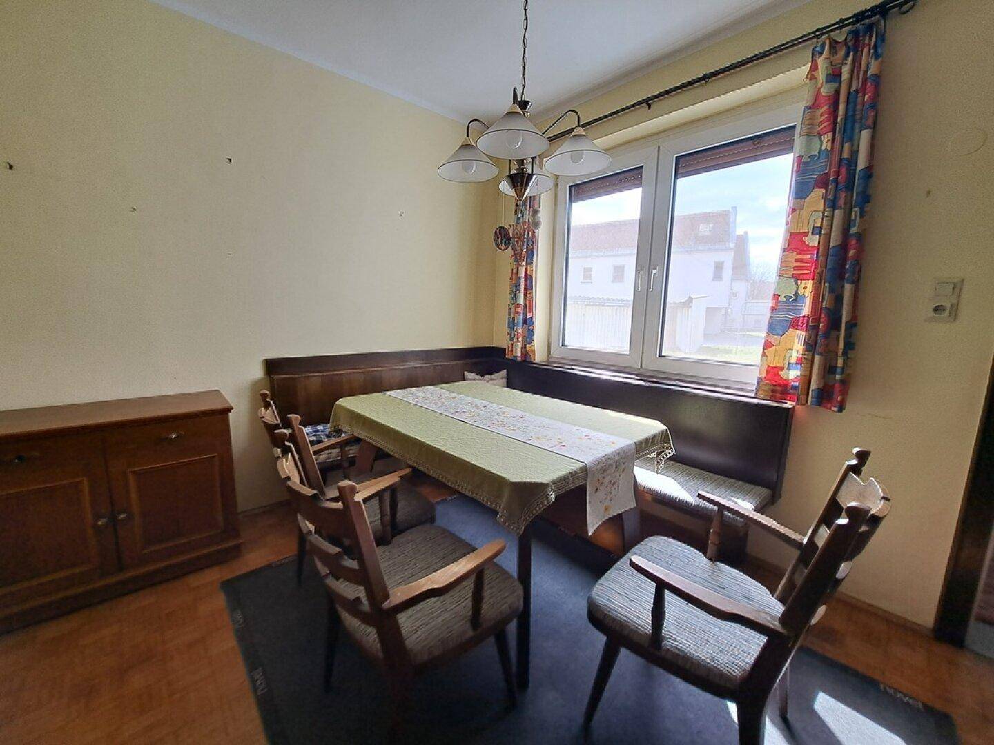 Gemütlicher Essbereich mit Holztisch, Eckbank und bunten Vorhängen am Fenster.