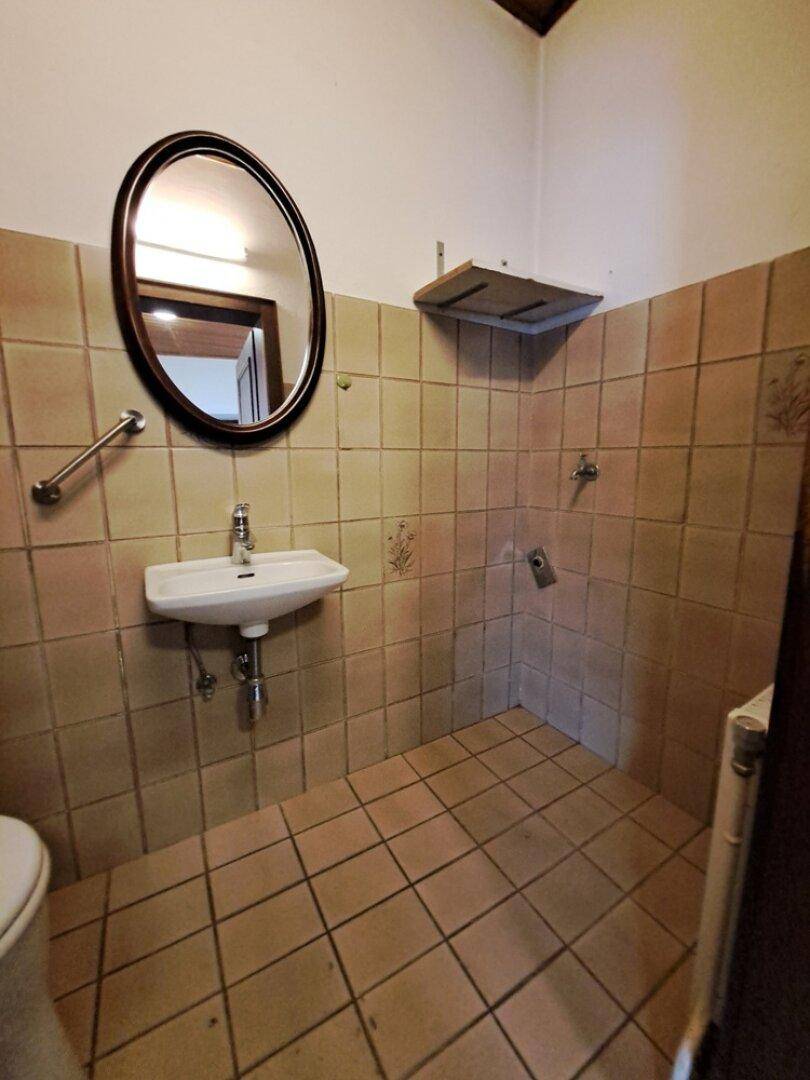 Einfaches Badezimmer mit beigefarbenen Fliesen, kleinem Waschbecken und ovalem Spiegel.