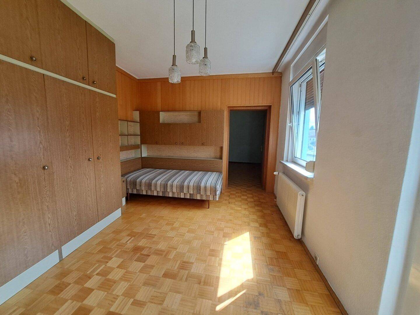 Schlafzimmer mit Einbauschränken, Holzvertäfelung, Parkettboden und einem Einzelbett.