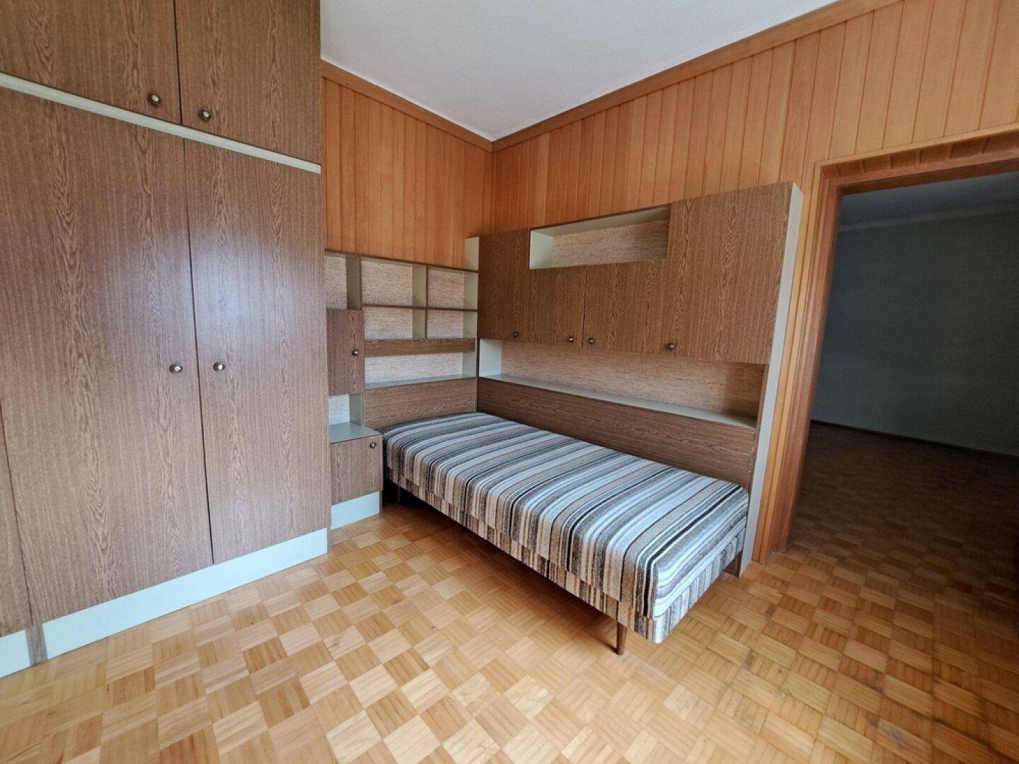 Gemütliches Schlafzimmer mit Holzvertäfelung, Einbauschränken und einem Einzelbett mit gestreifter Matratze.