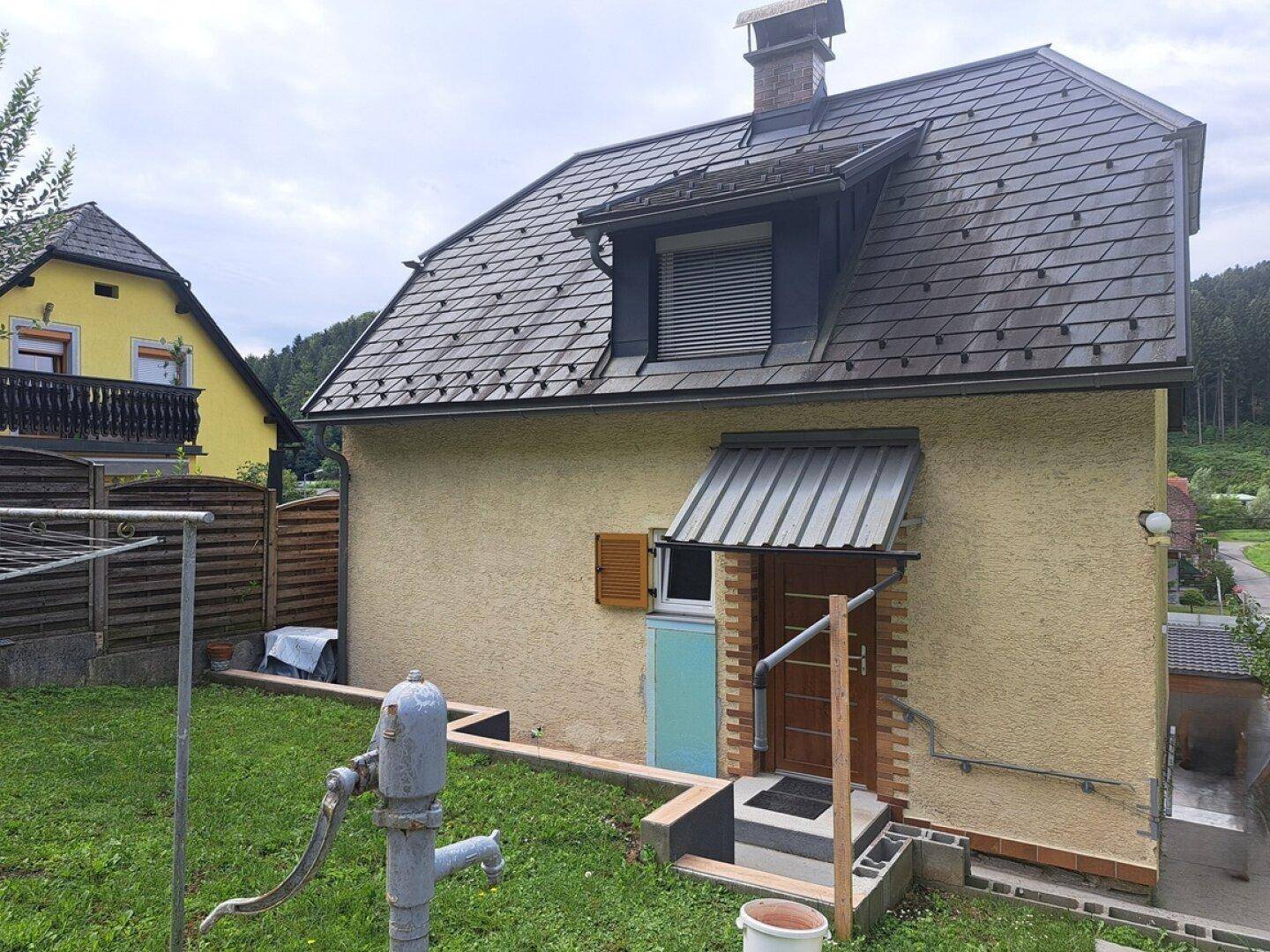 Seitenansicht des Hauses mit einem gepflegten Gartenbereich, alter Wasserpumpe und Wäscheleine.