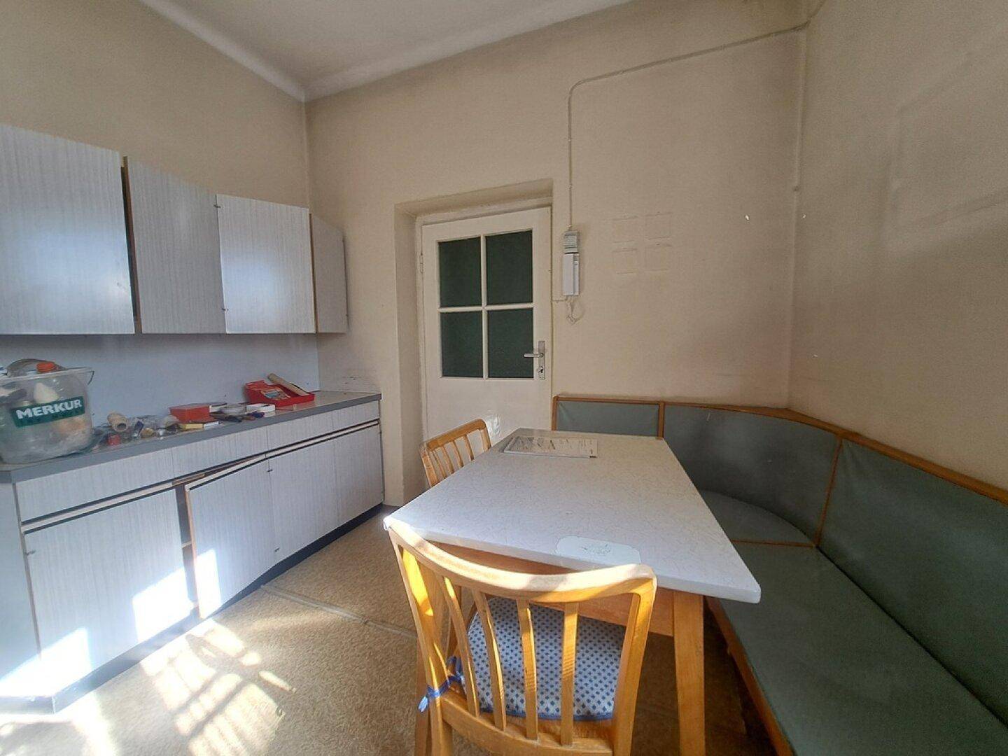 Küche mit einfacher Einrichtung, einer Essecke und einem Fenster, das viel Tageslicht hereinlässt.