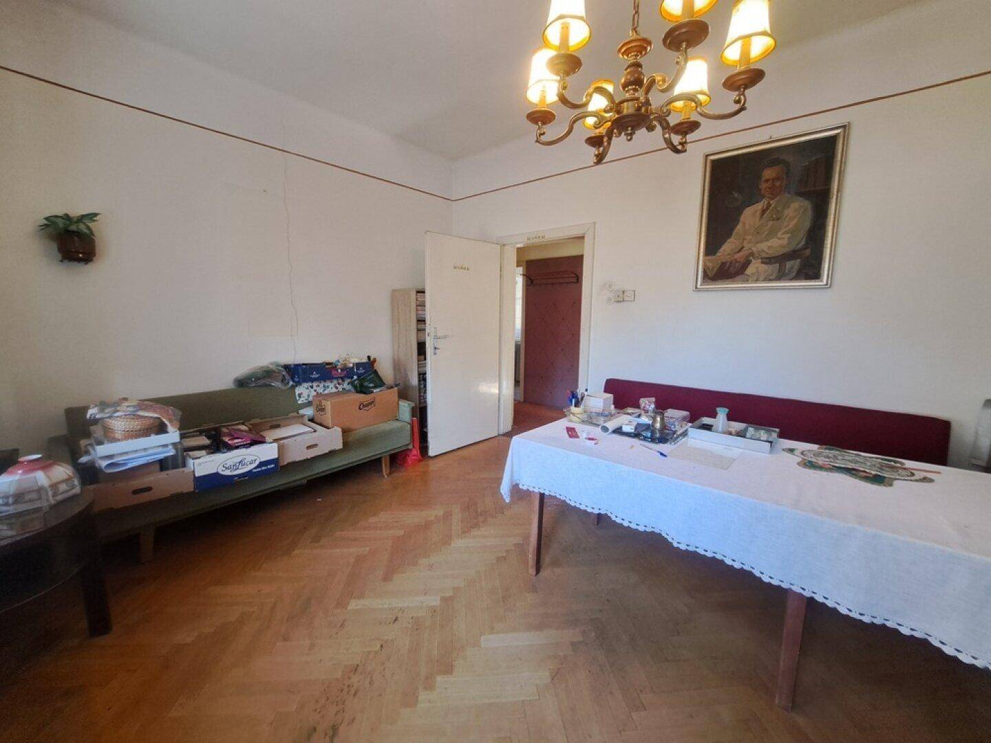 Geräumiger Wohn- und Essbereich mit Fischgrätparkett, Kronleuchter und traditionellen Möbeln.
