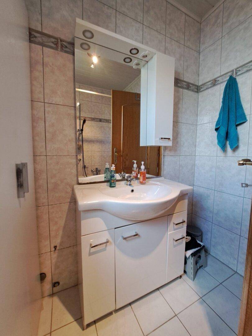 Badezimmer mit Waschtisch, Spiegelschrank und hellen Fliesen an Wänden und Boden.