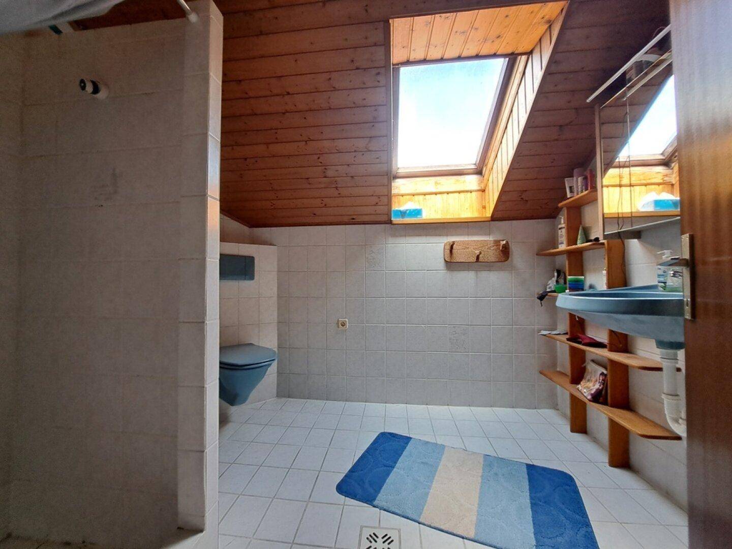 Badezimmer im Dachgeschoss mit Dachfenster, Toilette und Holzdeckenverkleidung.
