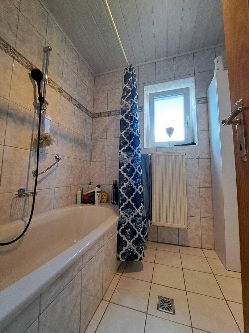 Gefliestes Badezimmer mit Badewanne, Duschvorhang und einem Fenster für Tageslicht.
