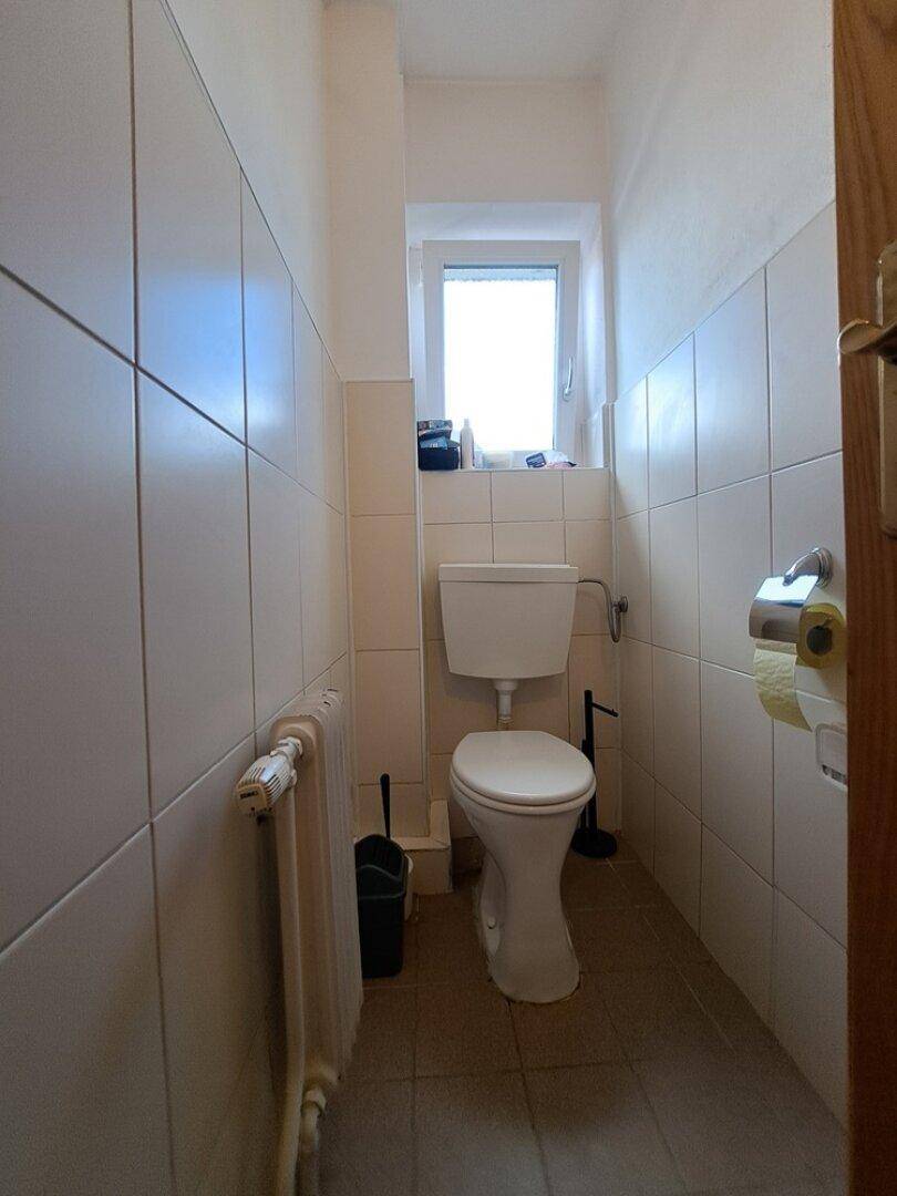 Kleines Gäste-WC mit Fenster, Toilette und hellen Wand- und Bodenfliesen.