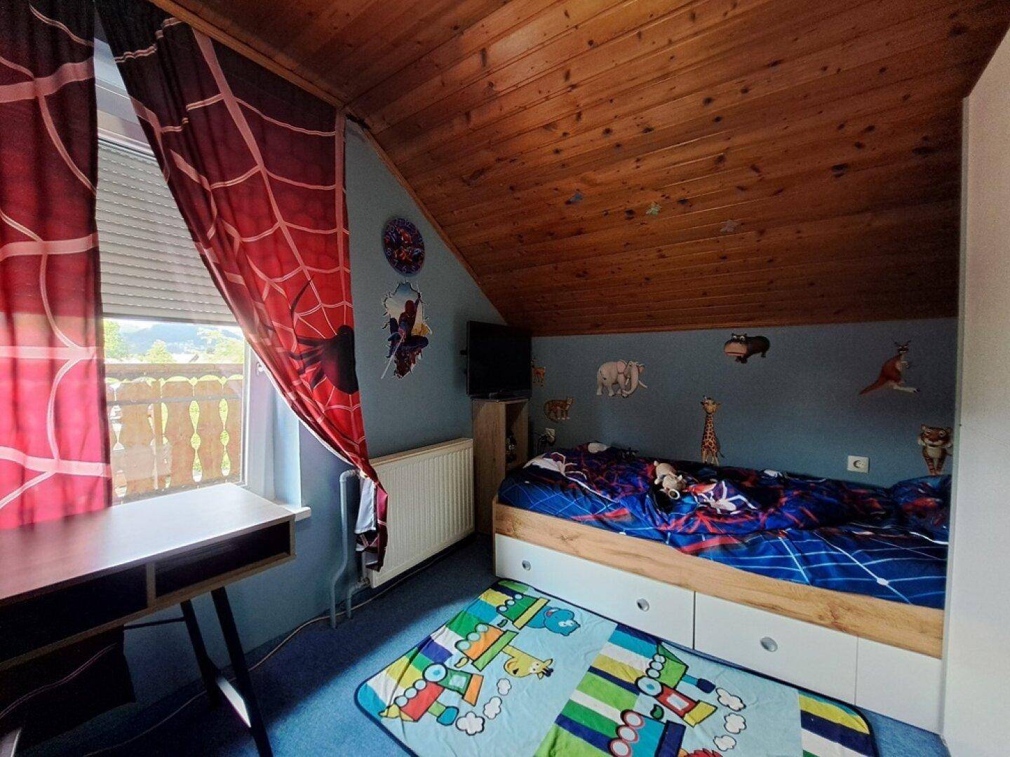 Kinderzimmer im Dachgeschoss mit Holzdecke, Fenster und bunter Dekoration.