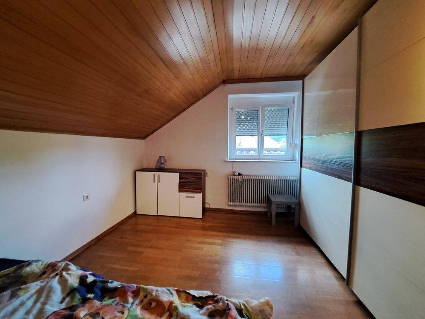 Helles Schlafzimmer im Dachgeschoss mit Holzdecke, Fenster und großem Kleiderschrank.