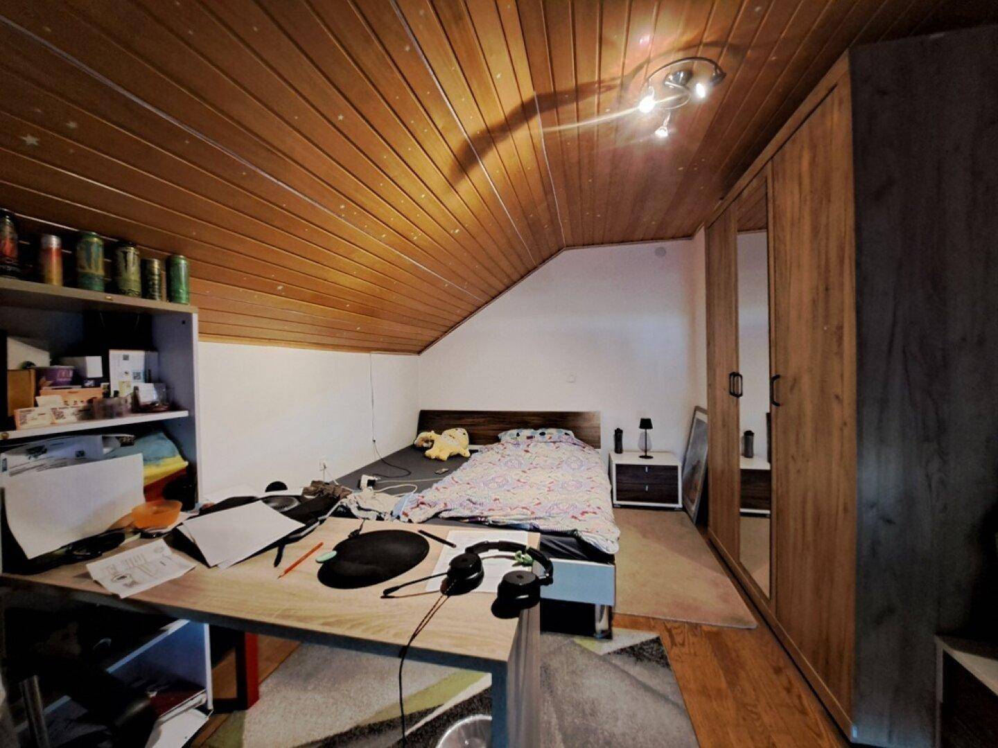 Schlafzimmer im Dachgeschoss mit Holzdeckenverkleidung, Bett und Kleiderschrank.