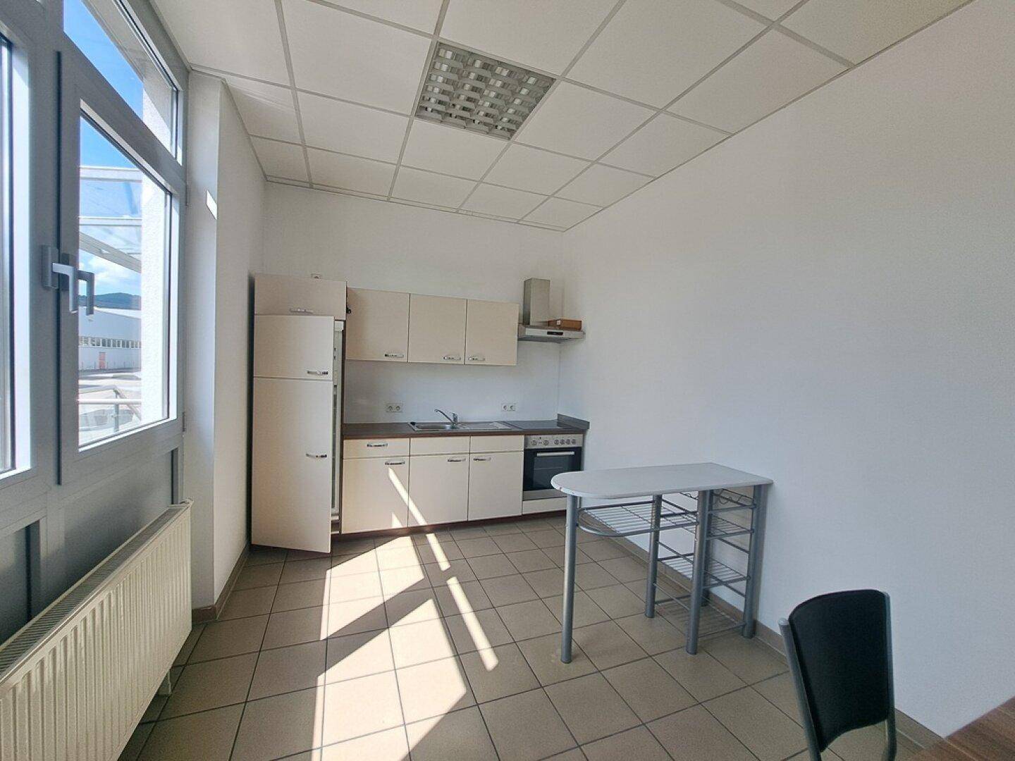 Kleine Küchenzeile mit hellen Schränken, Spüle, Herd und Kühlschrank, gut beleuchtet.