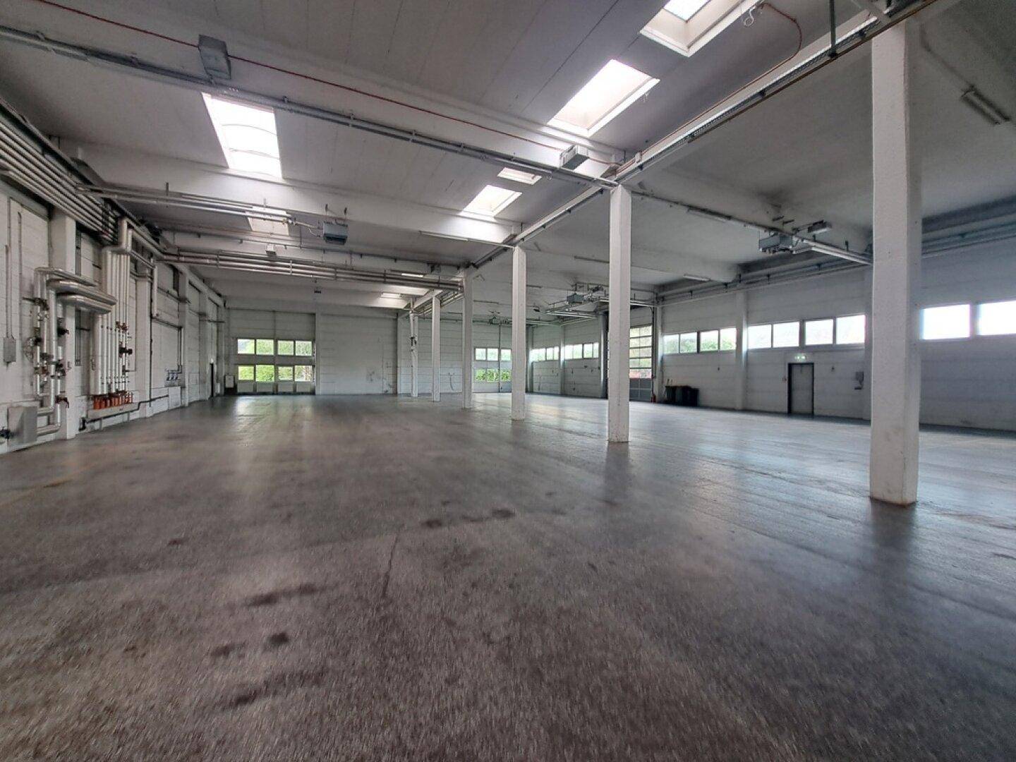 Weitläufige, leere Lagerhalle mit robustem Betonboden und hohen Decken, ideal für gewerbliche Nutzung.
