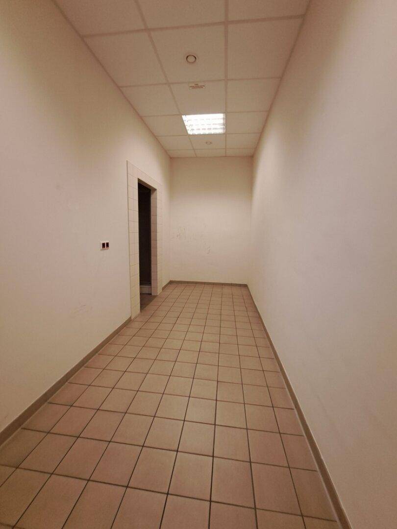 Schmaler Flur mit Fliesenboden, weißen Wänden und einer Tür am Ende, gut beleuchtet.