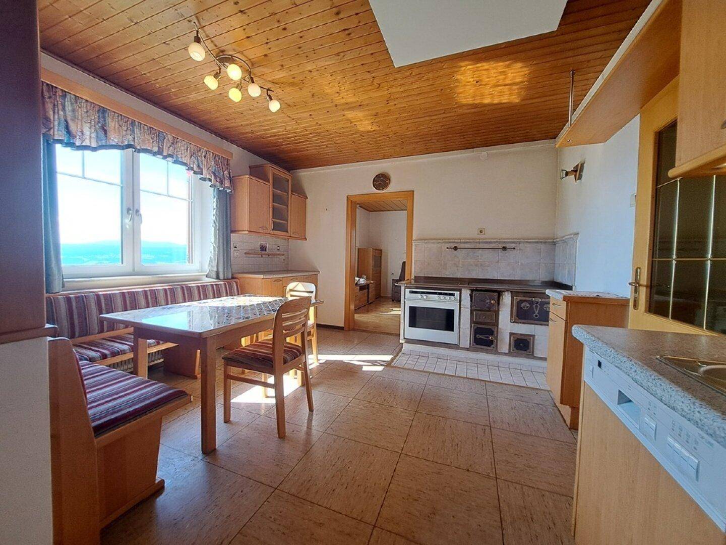 Rustikale Küche mit Holzdecke, Kachelofen und Blick auf die umliegende Landschaft.