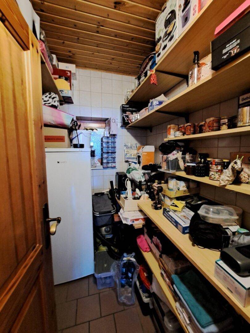 Praktische Speisekammer mit Regalen, Kühlschrank und gefliestem Boden unter einer Holzdecke.