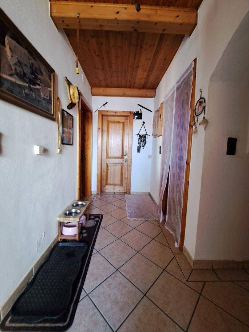 Traditioneller Flur mit Holzbalkendecke, Fliesenboden und rustikalen Holztüren, der zu weiteren Räumen führt.