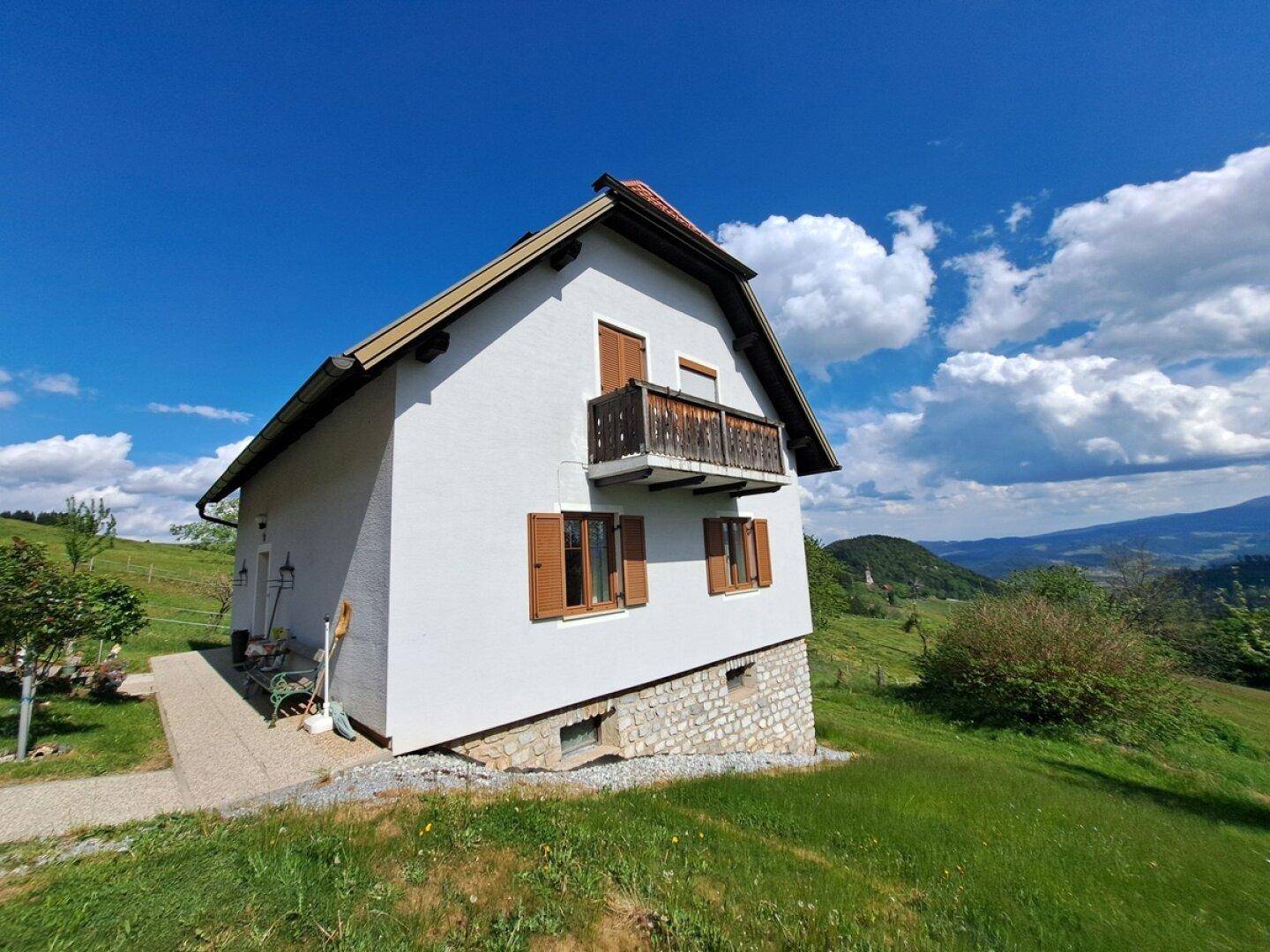 Seitenansicht des Hauses mit kleinem Balkon und Blick auf die hügelige Landschaft.