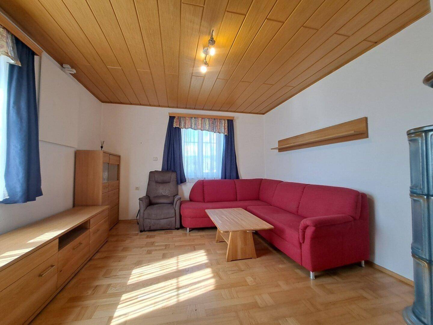 Helles Wohnzimmer mit Holzdecke, Parkettboden und rotem Ecksofa.