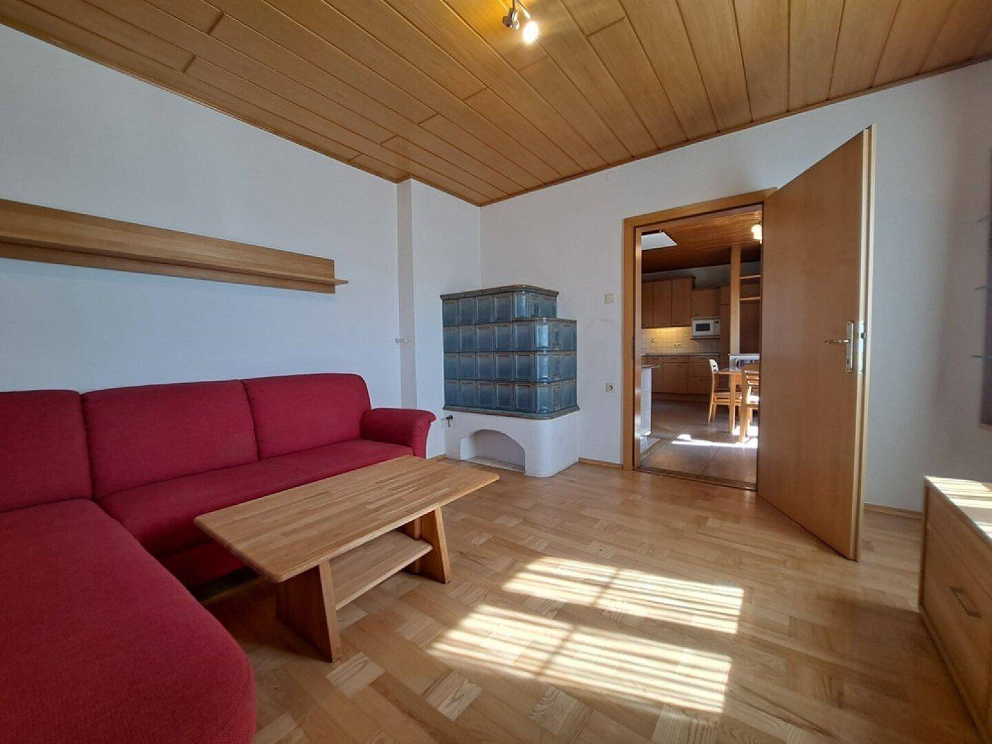 Wohnzimmer mit traditionellem Kachelofen, Parkettboden und Zugang zur Küche.