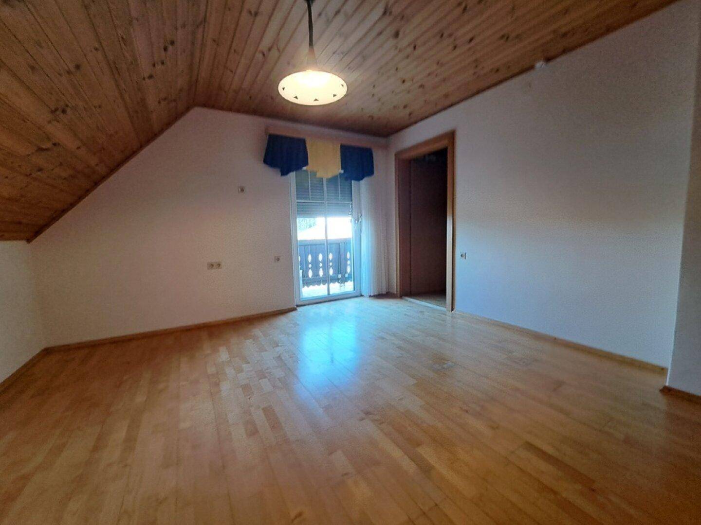 Helles Schlafzimmer im Dachgeschoss mit Holzboden und Zugang zum Balkon.