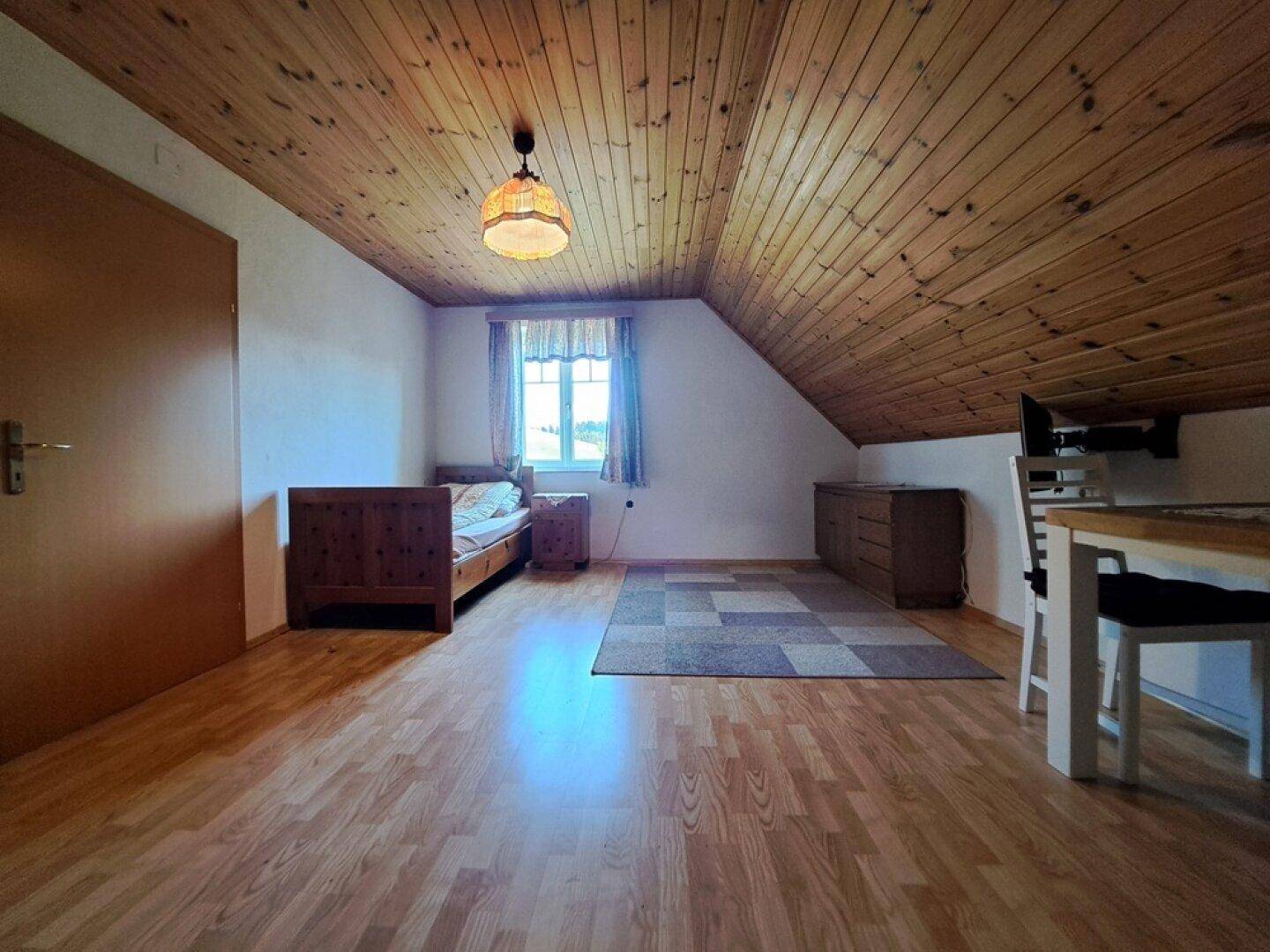 Geräumiges Schlafzimmer im Dachgeschoss mit Holzdecke und Holzboden.