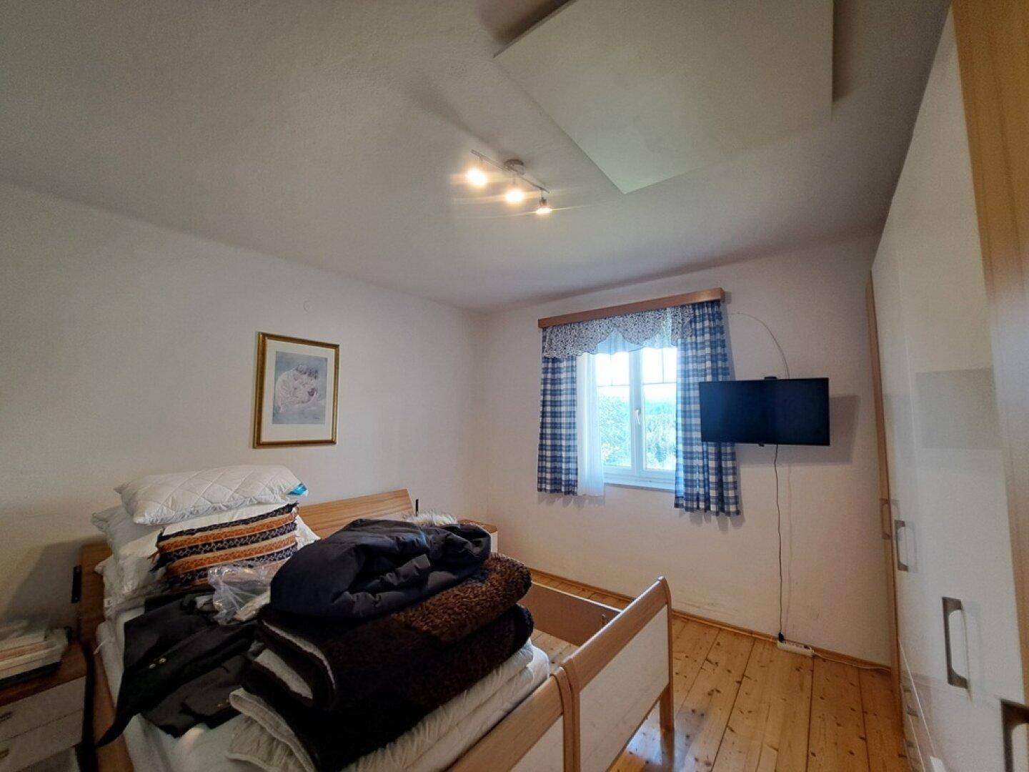 Schlafzimmer mit Holzboden, Fenster und einfacher Einrichtung.