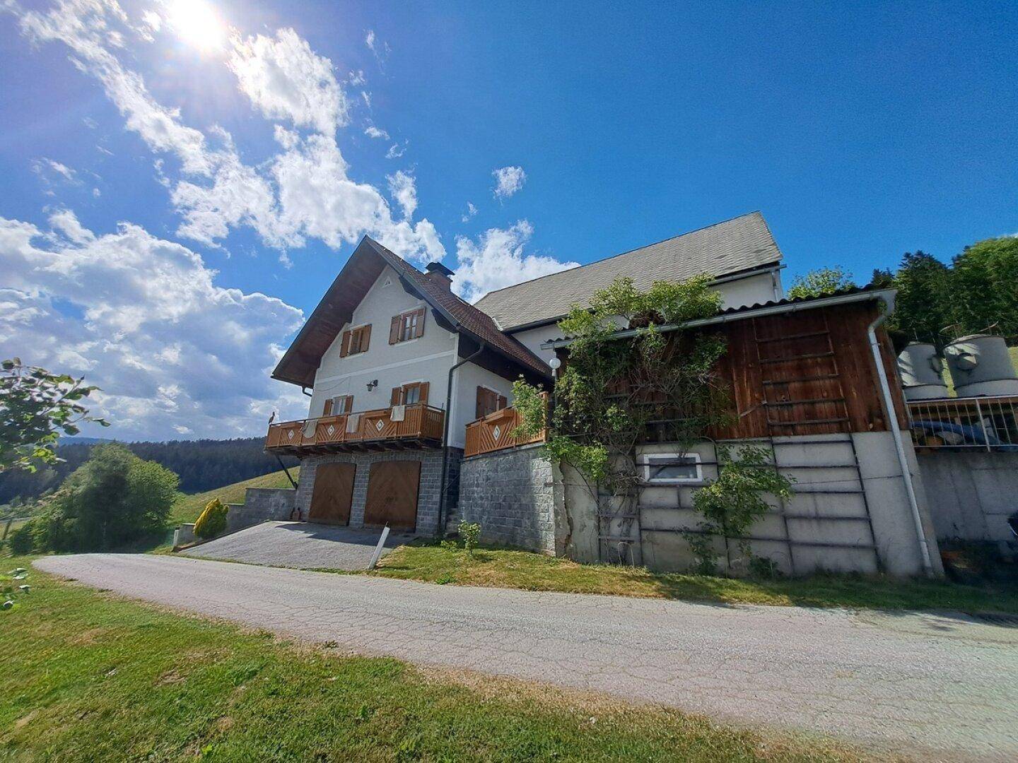 Hausfassade mit Balkonen und Garagen in ländlicher Umgebung unter blauem Himmel.