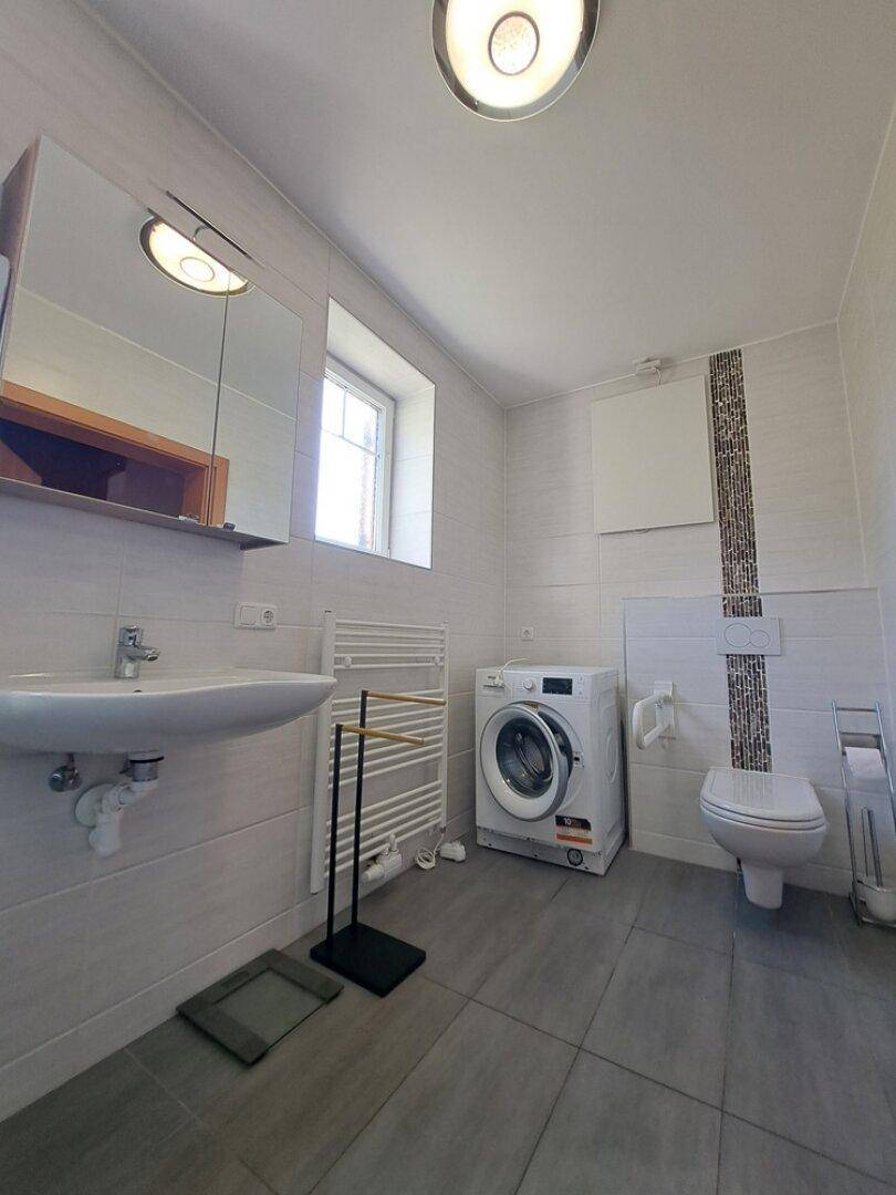 Modernes Badezimmer mit Waschmaschine, WC, Waschbecken und beheiztem Handtuchhalter.