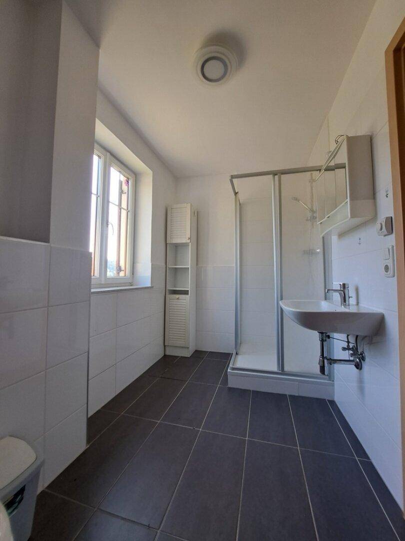 Helles Badezimmer im Dachgeschoss mit Dusche, Waschbecken und Fenster.