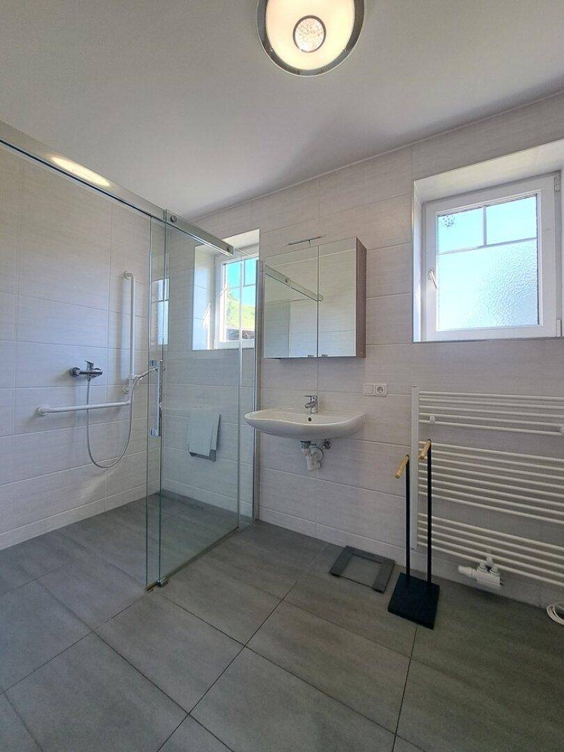 Helles Badezimmer mit ebenerdiger Dusche, Waschbecken und Fenster.