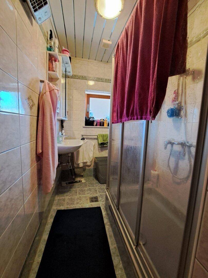 Badezimmer mit Duschkabine, Waschbecken, gefliesten Wänden und einer Holzpaneeldecke.