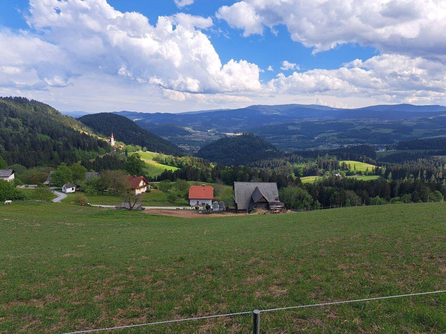 Weitläufige Aussicht auf eine ländliche Gegend mit Häusern, Wäldern und Bergen unter blauem Himmel.