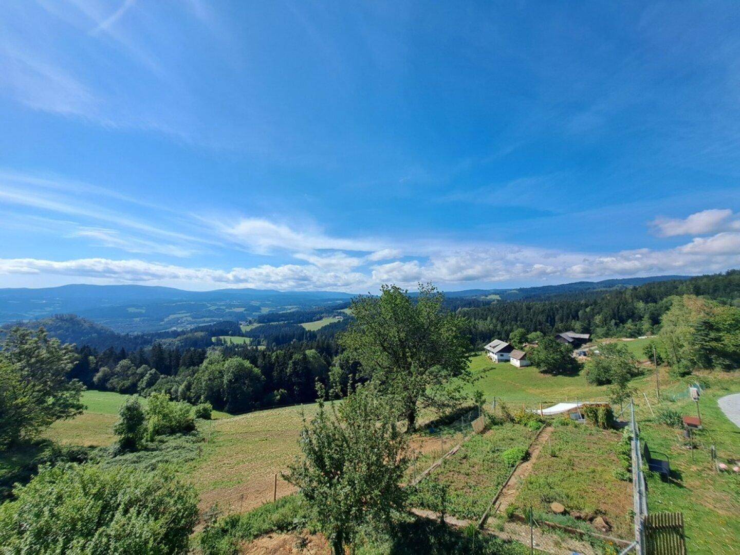 Großer Gartenbereich mit Anbauflächen, Bäumen und einem weiten Blick auf die umliegende Landschaft.