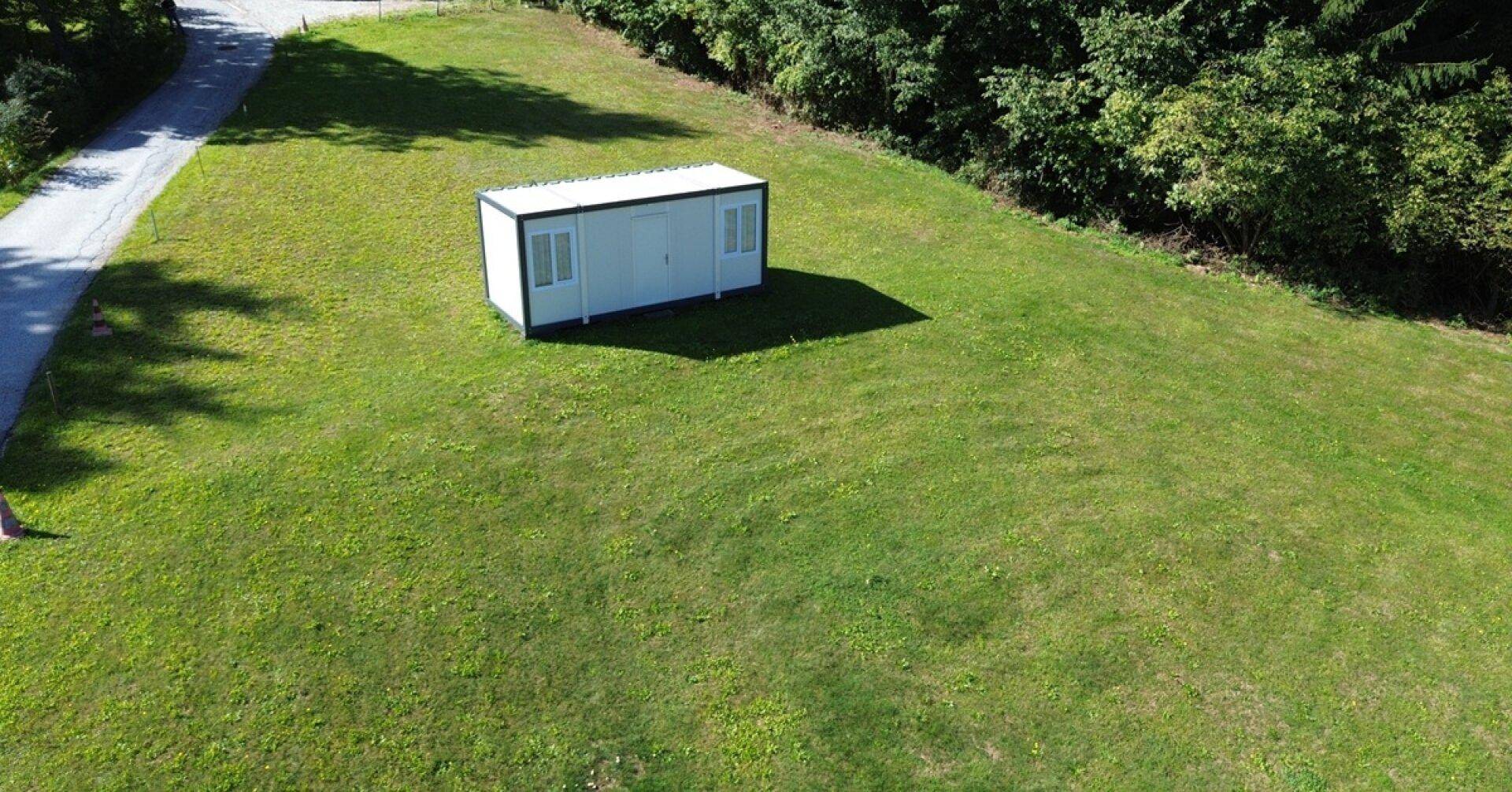 Übersicht des grünen Grundstücks mit einem modernen Containergebäude und Zufahrtsweg.