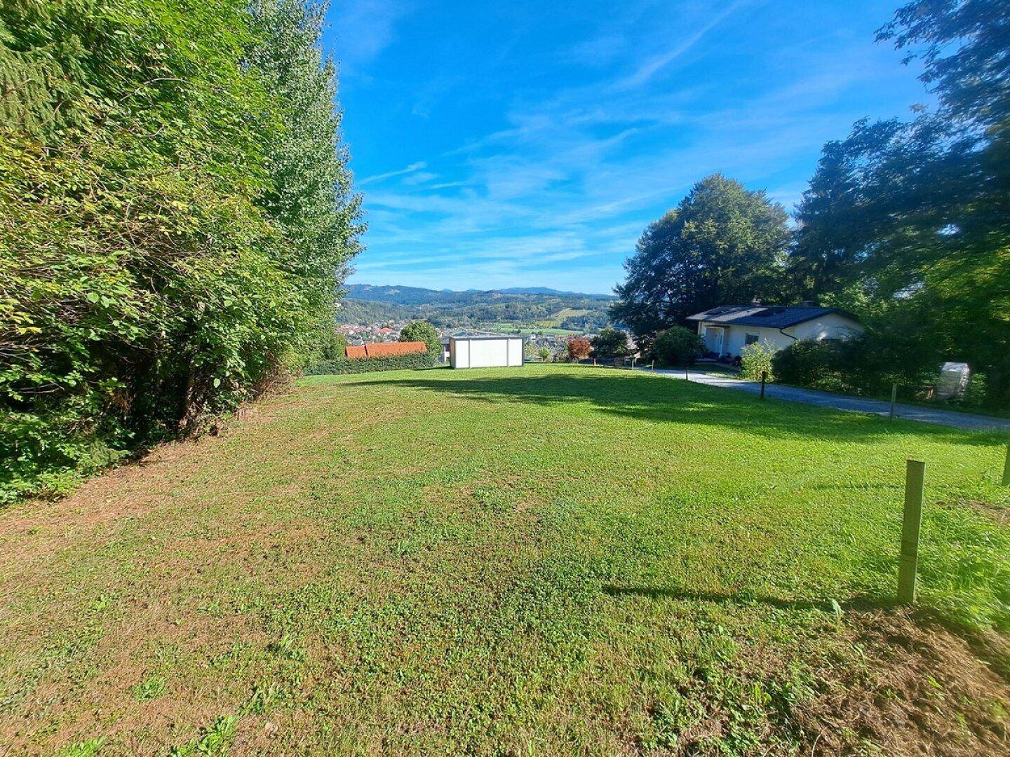 Grünes Grundstück mit weitem Blick auf die Landschaft und eine kleine Siedlung in der Ferne.